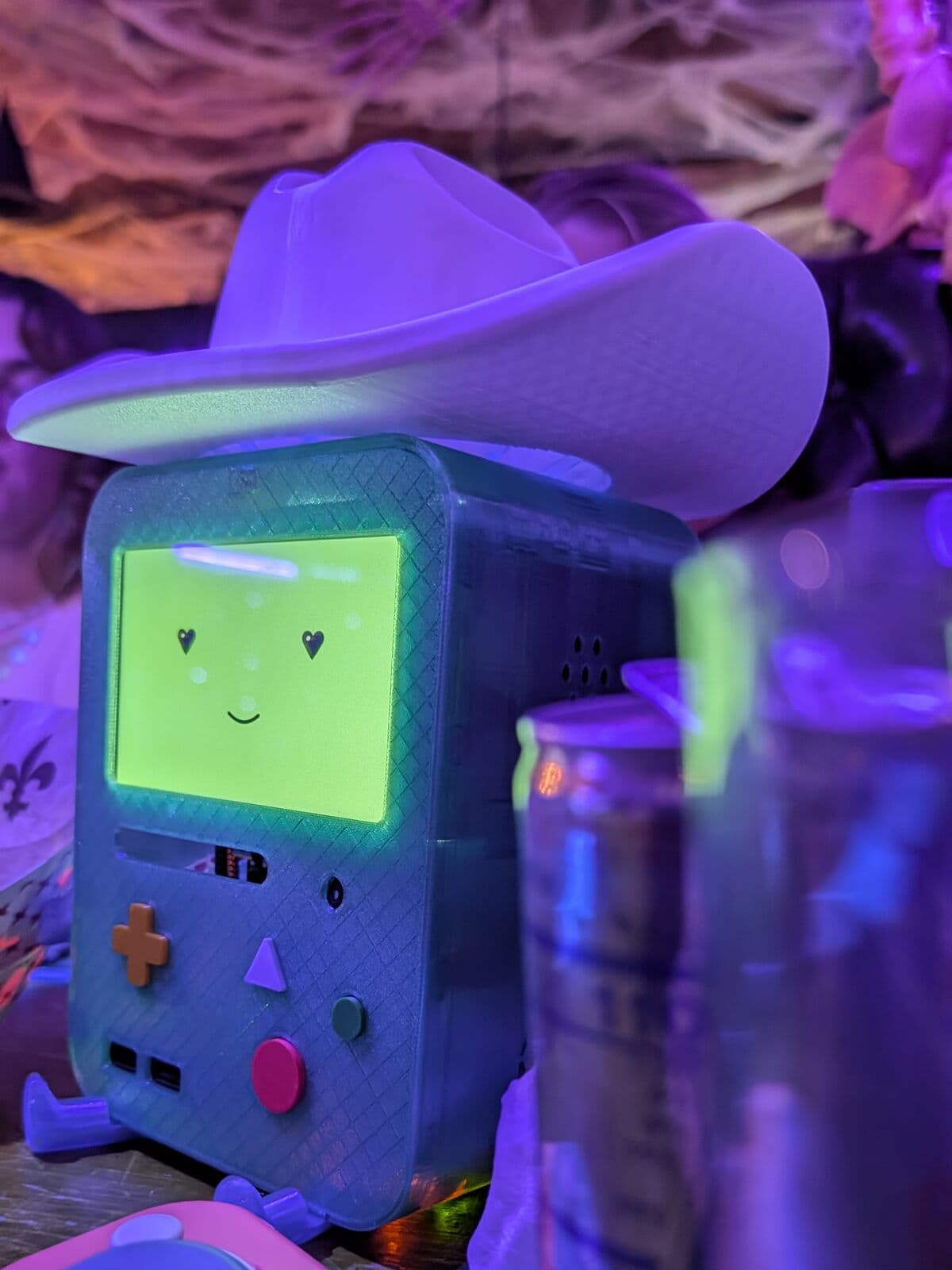 Beau, a small teal robot Matt built, wearing a white cowboy hat on a night out under purple lights.